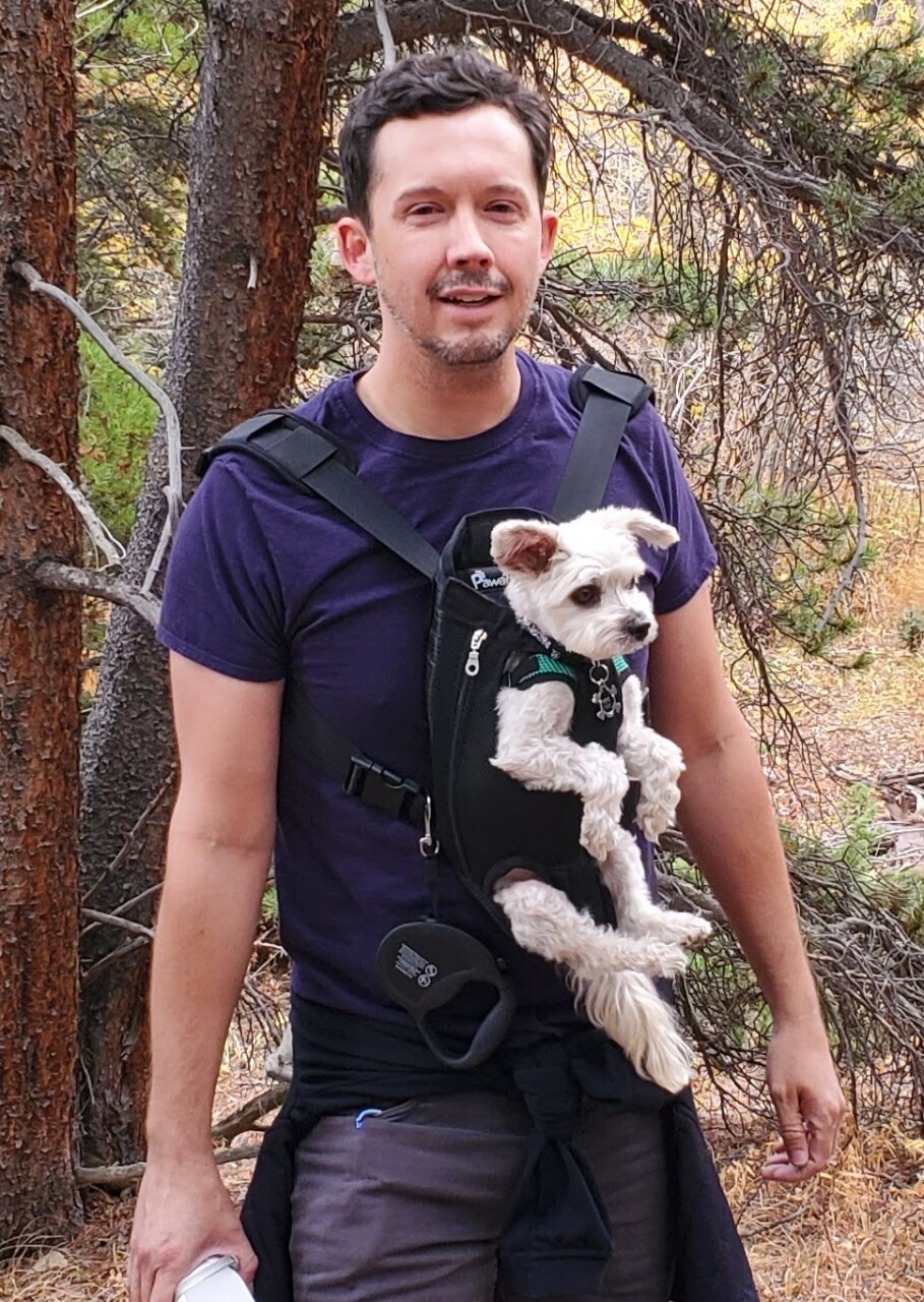 Executive Director, Jackson Bartlett, on a hiking trail with his dog, Pepe, strapped to his chest in a dog carrier.