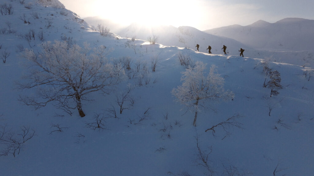 A group hikes along a snowy mountain ridge in single file
